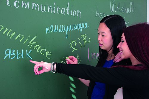 Zwei Studentinnen stehen vor einer Tafel mit Begrüßung in verschiedenen Sprachen