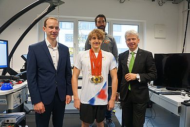 Paralympics-Sieger David Kratochvíl (Mitte) präsentiert seine Medaillen gemeinsam mit Prof. Dr. Christian Schmidkonz, Leiter des ZLS, (links), Christian Wolf von der hohpe GmbH (hinten) und Hochschulpräsident Prof. Dr. Clemens Bulitta